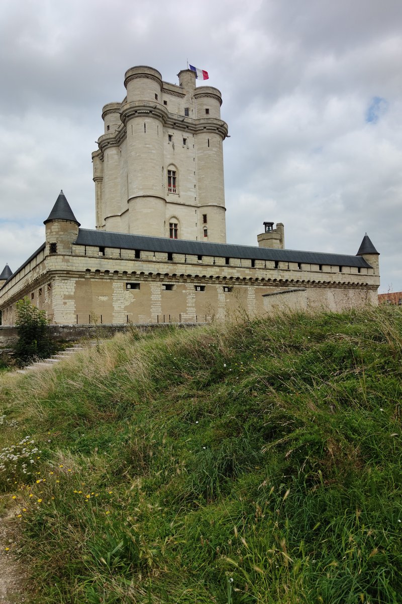 El imponente torreón del Château de Vincennes se alza sobre su muralla cortina y el foso seco bajo una luz diáfana: la fortaleza medieval fortificada más alta de Europa, con la Sainte-Chapelle al fondo. Vincennes, en el límite oriental de París, Francia.